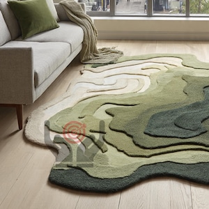 May include: A large, green and beige area rug with a topographical design. The rug features varying shades of green and beige, creating a layered effect. The rug is placed on a light-coloured wooden floor, near a grey sofa with green cushions.