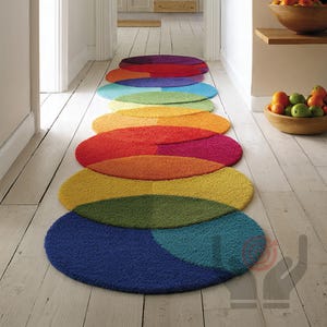 Könnte beinhalten: Eine Reihe farbenfroher, oval geformter Teppiche, die in einem Flur angeordnet sind. Die Teppiche sind in den Farbtönen Rot, Orange, Gelb, Grün, Blau und Lila gehalten. Die Teppiche bestehen aus einem weichen, strukturierten Material und verleihen dem Raum eine lebendige Note.