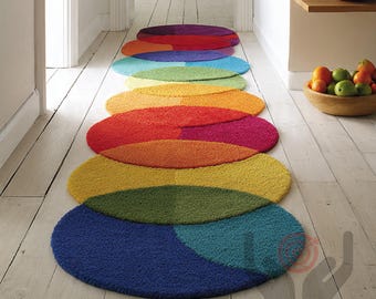 Puede incluir: Una serie de alfombras ovaladas y coloridas dispuestas en un pasillo. Las alfombras son en tonos de rojo, naranja, amarillo, verde, azul y morado. Las alfombras están hechas de un material suave y texturizado y añaden un toque vibrante al espacio.