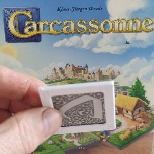 Puede incluir: Una ficha de juego de mesa Carcassonne, de color gris y blanco, con un diseño curvo.