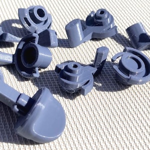 May include: A collection of seven small, grey, 3D-printed plastic mechanical components. Each piece features a circular base with a central hole, a protruding arm, and a curved, solid end section. The parts exhibit visible layer lines from the printing process.
