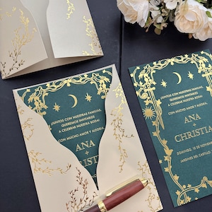 May include: A dark green wedding invitation card with gold foil celestial and floral motifs, featuring the text 'Juntos con nuestras familias, queremos invitarles a celebrar nuestra boda', 'Ana + Christian', and date details, tucked into a cream envelope.