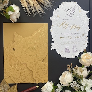 May include: A gold-colored envelope with an embossed floral design and a white, oval-shaped wedding invitation card featuring gold foil lettering. The text includes the names Kathy and Philip, the date Dec 13 2025, and the location MGM Cotai Level 3 Ballroom.