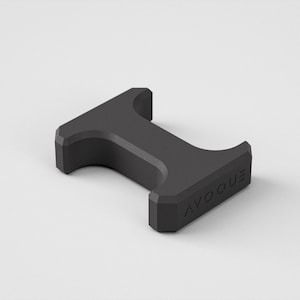 May include: A dark grey, geometric bottle opener with the word "AVOQUE" printed on the side. The opener has a T-shape with curved indentations on the top and bottom. The object is set against a plain white background.