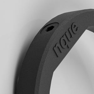 May include: Close-up of a black, textured, curved object with the word "nove" embossed on its surface. A small hexagonal hole is visible near the top. The object has a matte finish and appears to be made of a solid material.