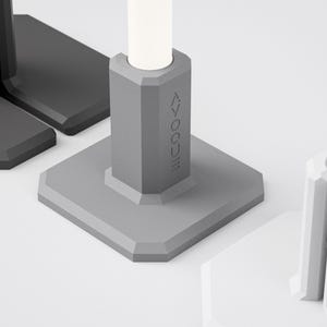 Op de afbeelding: Close-up van verschillende geometrische, grijze en zwarte objecten. Eén object heeft het woord "VOQUE" op de zijkant gedrukt. De objecten hebben een vierkante basis en een cilindrische bovenkant. De objecten staan op een wit oppervlak.