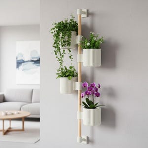 Könnte beinhalten: Ein vertikaler Wand-Pflanzenhalter mit vier weißen, geriffelten Pflanzgefäßen. Die Gefäße enthalten verschiedene grüne Pflanzen und lila Orchideen. Der Halter hat eine helle Holzstange und weiße Befestigungselemente, was eine moderne, minimalistische Ästhetik schafft.