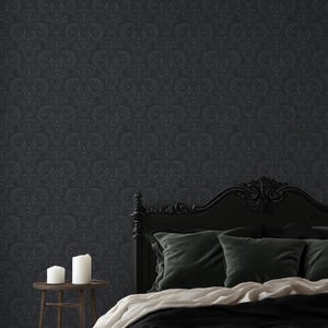 May include: Dark grey damask wallpaper covers the wall behind a black bed frame. The bed has dark green velvet cushions and a white blanket. A small wooden side table holds two white candles.
