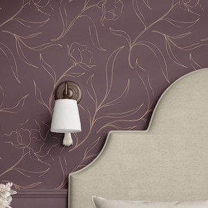 Può includere: Scena di camera da letto con carta da parati floreale color prugna con contorni dorati. Un paralume bianco con nappa pende da un'applique in bronzo. Sono visibili anche una testiera e un cuscino beige.
