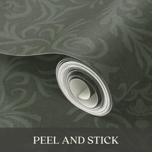 The product is a roll of peel-and-stick wallpaper with a dark, muted green base color. A subtle decorative pattern in a slightly lighter green shade runs across the surface. The material appears to have a smooth, matte texture. The wallpaper is shown in its rolled form, ready for unrolling and application.