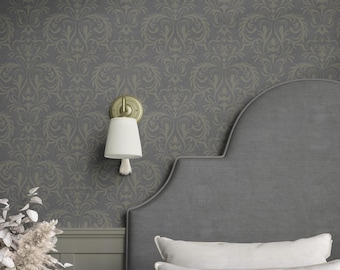 May include: A wall-mounted light fixture with a brass-toned circular base and a white, pleated, conical shade featuring a small white tassel. The light is positioned against a dark gray wallpaper with a repeating light gray damask pattern.