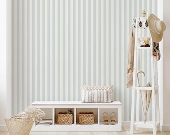 May include: A white wooden entryway bench with four open cubbies containing two woven baskets, topped with a patterned pillow. Beside it stands a white wooden coat rack holding a beige hat, a tan scarf, and a beige umbrella, against striped wallpaper.