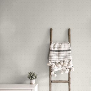Può includere: Una scala in legno rustico con una coperta color crema a righe nere e nappe. La coperta è drappeggiata sulla scala. Una piccola pianta in vaso è su un mobile bianco. Il muro è verde chiaro con piccoli punti distanziati.
