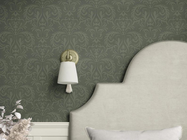 This wall-mounted sconce features a textured cream-colored fabric shade in a cylindrical form tapering subtly toward its open base. A single tassel extends from the shade’s lower center. The supporting arm and wall plate are metal finished in a brushed brass-like tone.