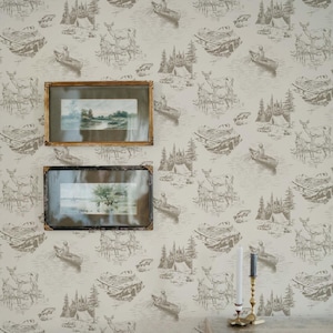 May include: A wall with a repeating pattern of deer, canoes, and camping scenes in shades of brown and beige. Two framed landscape paintings hang on the wall. A brass candle holder with two candles sits on a wooden surface.
