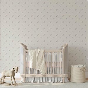 May include: A nursery scene featuring a cream-colored crib with a draped blanket and skirt. A wooden rocking horse and a woven basket are nearby. The wallpaper has a repeating floral pattern in pink and gray.