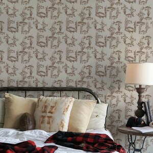 May include: A bedroom with a bed featuring beige pillows and a red and black plaid blanket. The wall is decorated with wallpaper displaying a repeating pattern of brown fish and aquatic plants. A wooden lamp and side table are also present.