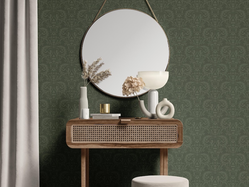 The image shows a round mirror with a slender metallic frame in a brushed gold finish. Below it sits a rectangular wooden console table with a woven rattan front panel and four slender tapered legs. In front of the table is a cylinder-shaped stool featuring a smooth beige upholstered top and a vertically pleated fabric skirt around its lower half.