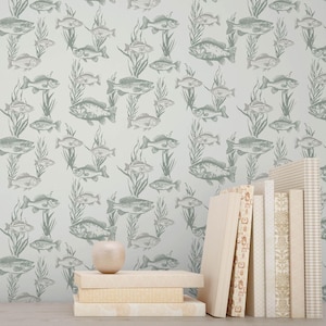 May include: A pale blue wallpaper featuring a repeating pattern of fish and seaweed in grey and green tones. A collection of books with beige and patterned covers are stacked on a wooden surface, with a decorative apple.