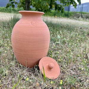 Op de afbeelding: Een terracotta pot met een deksel. De pot is lichtbruin van kleur en heeft een gladde, ronde vorm. Het deksel is ook van terracotta en heeft een klein knopje bovenop.