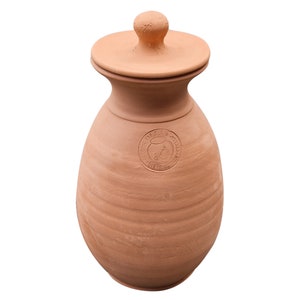 Könnte beinhalten: Eine Terrakotta-Vase mit Deckel, die ein rundes Logo mit einem stilisierten Bild eines Vogels und dem Text "DIST. BY" in einem braunen, weißen und grünen Farbschema zeigt.