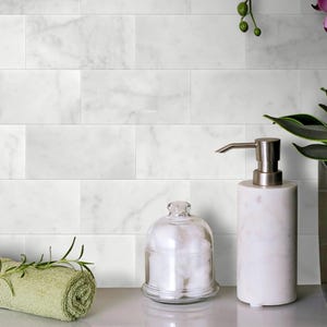 May include: White marble tile backsplash with a white ceramic soap dispenser and a glass jar with cotton balls on a white countertop.