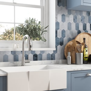 May include: A white farmhouse kitchen sink with a chrome faucet and a window behind it. The backsplash is a blue and gray geometric tile pattern.