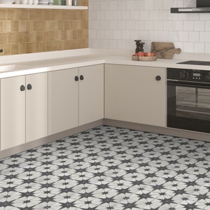 May include: A kitchen with white subway tile backsplash, beige cabinets, and a black oven. The floor is tiled with a black and white geometric pattern.