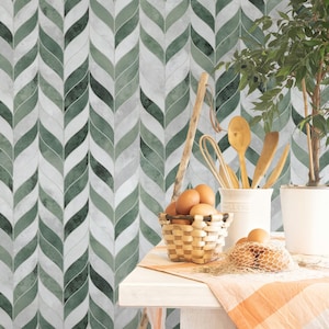 May include: A kitchen scene featuring a green and white leaf-patterned tile backsplash. A small basket of brown eggs sits on a white table, along with wooden utensils in a white ceramic container and a small potted plant.