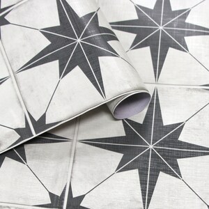 May include: Close-up of a roll of peel and stick floor tiles featuring a repeating pattern of black eight-pointed stars on a white background.