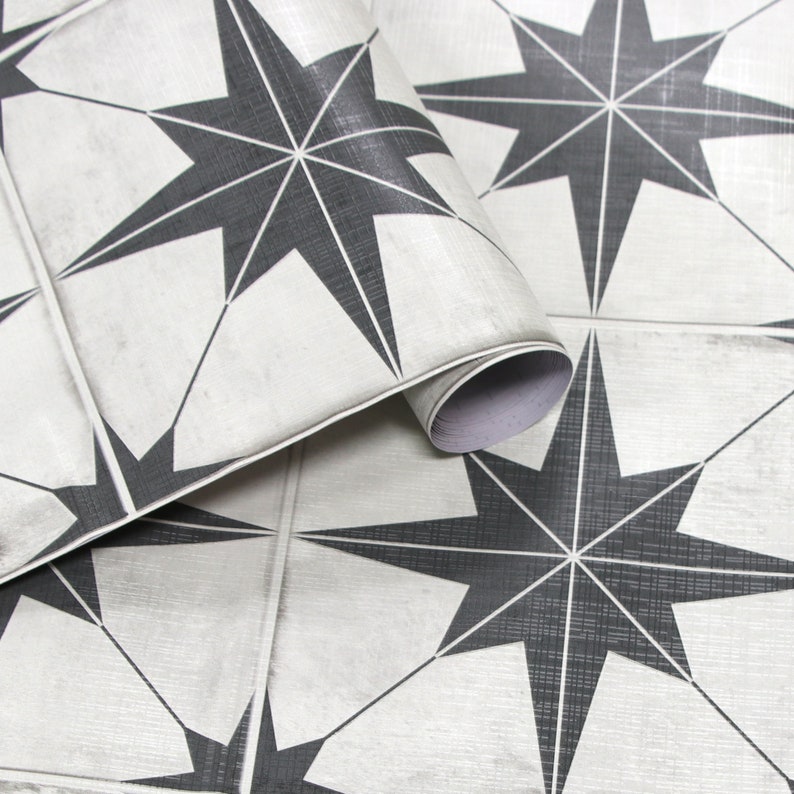 May include: Close-up of a roll of peel and stick floor tiles featuring a repeating pattern of black eight-pointed stars on a white background.