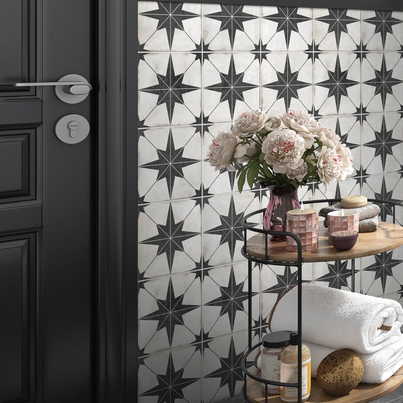 May include: A black and white patterned tile with a star design. A metal cart with two shelves holds a bouquet of pink flowers, towels, and bath products.