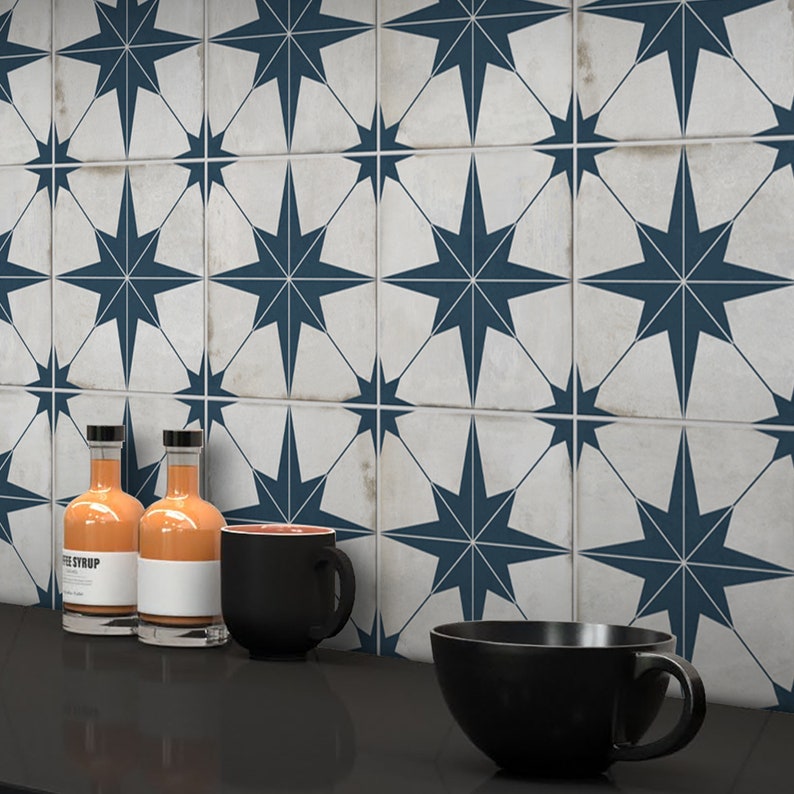 May include: A kitchen countertop with a white and blue star patterned tile backsplash. There are two glass bottles with orange liquid, a black mug, and a black bowl on the countertop.