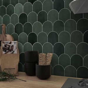 May include: Green ceramic tiles in a fish scale pattern with white grout lines. Three black ceramic mugs and a stack of crackers are on a wooden counter in front of the tiles.