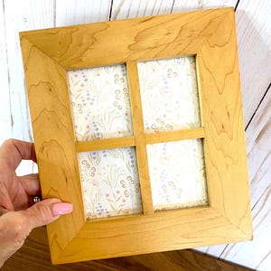 Può includere: Una cornice quadrata in legno con finitura in legno chiaro. La cornice è divisa in quattro sezioni, ognuna delle quali mostra una carta a motivi floreali con fiori lavanda e rosa. La cornice è tenuta in mano con smalto rosa.