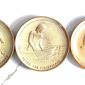 Può includere: Tre piatti in ceramica con immagini in rilievo di persone e testo. I piatti sono beige con accenti marroni. Il primo piatto presenta una donna che cucina e il testo "Martha la casalinga". Il secondo piatto presenta un uomo che pesca e il testo "Pietro il pescatore". Il terzo piatto presenta una donna che cuce e il testo "Dorcas la sarta".