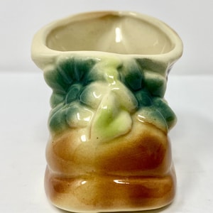 Może przedstawiać: Mały ceramiczny pojemnik na rośliny w kształcie brązowego buta z zielonymi i żółtymi detalami kwiatowymi.