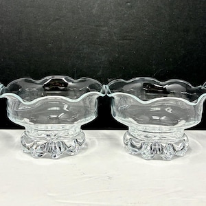 May include: Four clear glass dessert bowls with scalloped rims and decorative pedestal bases. The bowls are arranged in a row, showcasing their elegant design and clarity. Perfect for serving desserts or small portions.