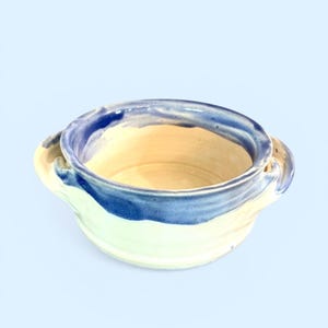 Pode incluir: Uma tigela de cerâmica feita à mão com interior creme e exterior azul e branco. A tigela tem duas pequenas alças e é ideal para servir sopas ou ensopados. A tigela tem aproximadamente 15 cm de diâmetro e 7,6 cm de altura.