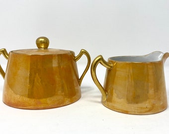 Jarra para crema y azucarero de cerámica color melocotón con asas doradas y tapa dorada, fabricada en Japón.