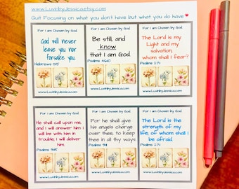 May include: A sheet of stickers with inspirational quotes from the Bible, featuring floral illustrations. The stickers are arranged in a grid, with text such as "God will never leave you nor forsake you." Two pens rest on the side.