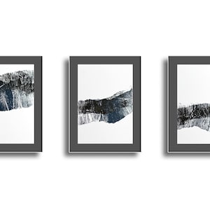 May include: Three framed abstract art prints. Each print features a textured, dark gray and blue horizontal band against a white background. The frames are dark gray, and the overall aesthetic is modern and minimalist.