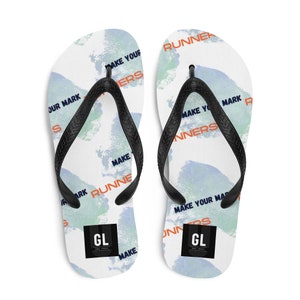 Könnte beinhalten: Ein Paar weiße Flip-Flops mit einem blauen und grünen Aquarell-Design. Die Flip-Flops haben schwarze Riemen und der Text "Make Your Mark Runners" wird auf den Riemen wiederholt. Der Text "GL" befindet sich in einem schwarzen Quadrat auf jedem Flip-Flop.