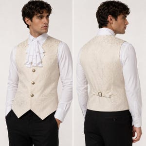 May include: A cream-colored vest with a subtle floral pattern, featuring three round gold buttons on the front, a pointed hem, and an adjustable strap with a metal buckle on the back. The vest is worn over a white long-sleeved shirt with a ruffled cravat.