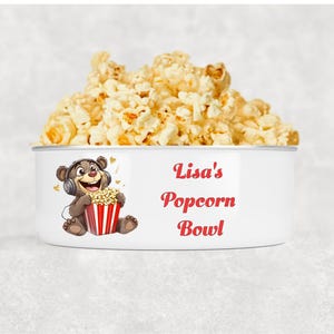 May include: A white popcorn bowl filled with popcorn. The bowl has a cartoon bear wearing headphones and holding a popcorn container. The text "Lisa's Popcorn Bowl" is written in red.
