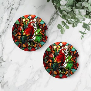 May include: Two round coasters with a stained glass design featuring a red and blue parrot perched on a branch with green leaves. The background is a colorful stained glass pattern.