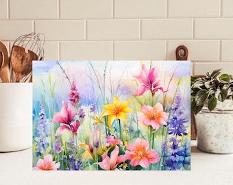 May include: A rectangular print featuring a watercolor painting of a vibrant wildflower meadow. The scene displays pink, yellow, and purple lilies alongside tall green grasses and slender stalks against a soft, light blue and white background.