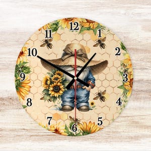 May include: Round wall clock featuring a whimsical gnome wearing a straw hat and denim overalls, holding sunflowers. The clock face has a honeycomb pattern, bees, and sunflower accents. Black clock hands point to the time.