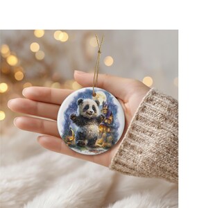 A hand holding a decorative ornament featuring a panda bear against a night sky background.