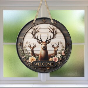 Op de afbeelding: Een ronde houten welkomstbord met een hertenfamilie. Het bord heeft een donkerbruine rand en een lichte houtnerf achtergrond. Het woord "WELCOME" staat onderaan. Het bord wordt opgehangen met een touw.